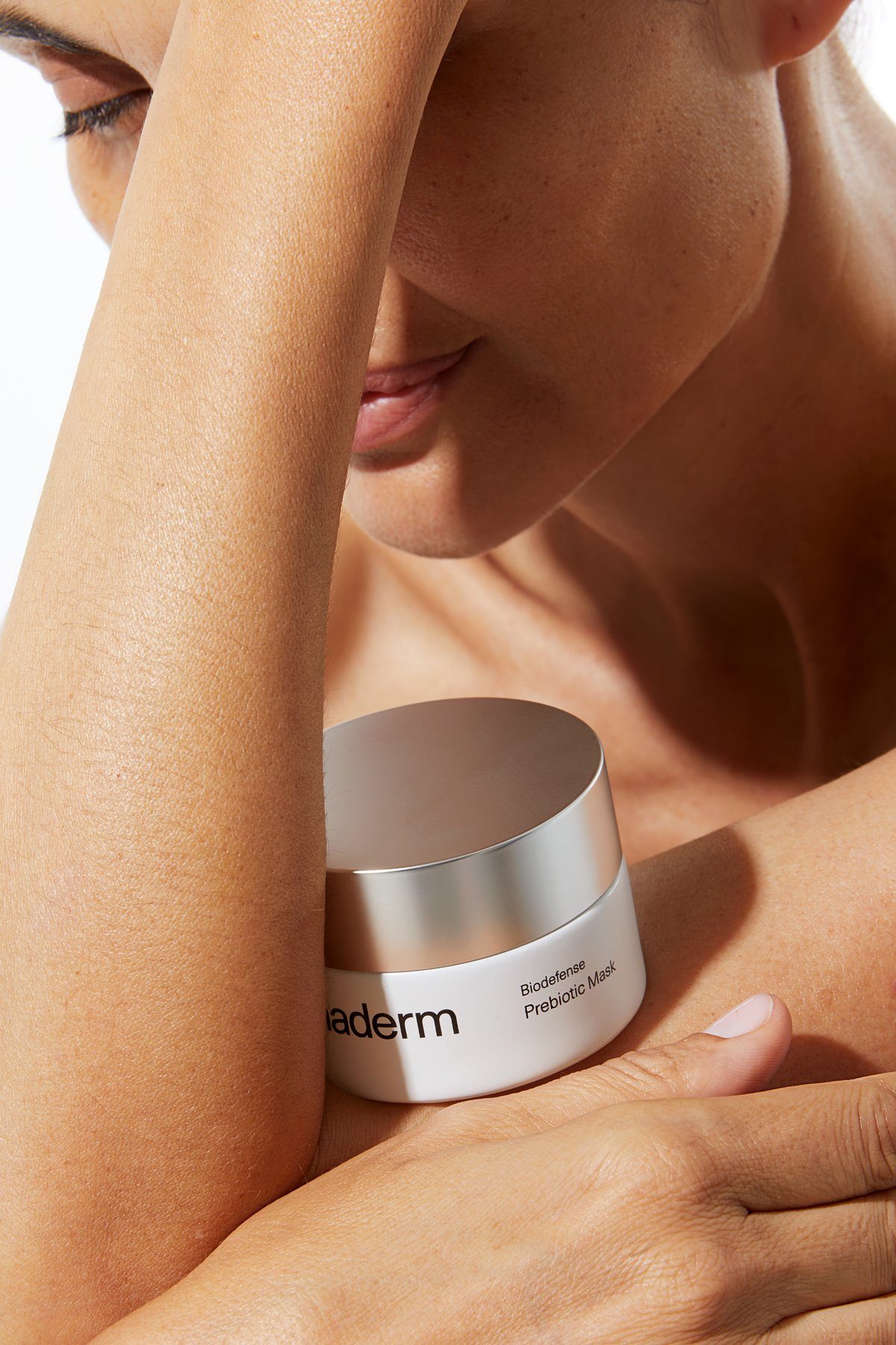 Woman resting her cheek on her arm, relaxed, with Biodefense cream nearby